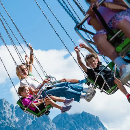 Familien auf einer Schaukel im Erlebnispark, Berge im Hintergrund