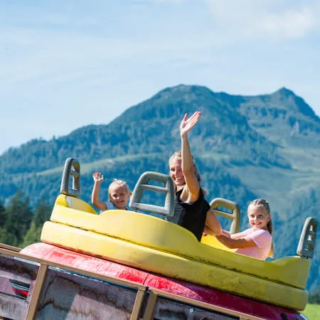 Familien im Erlebnispark mit Bergen im Hintergrund.