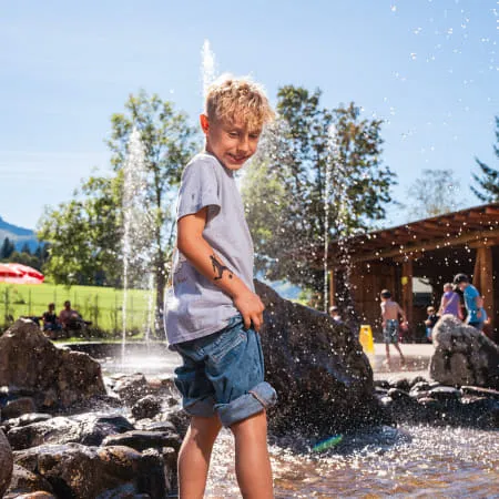 Junge steht im Wasser mit Spritzfontänen im Erlebnispark
