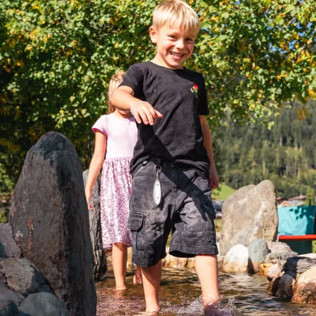 Junge watet fröhlich durch einen kleinen Wasserlauf